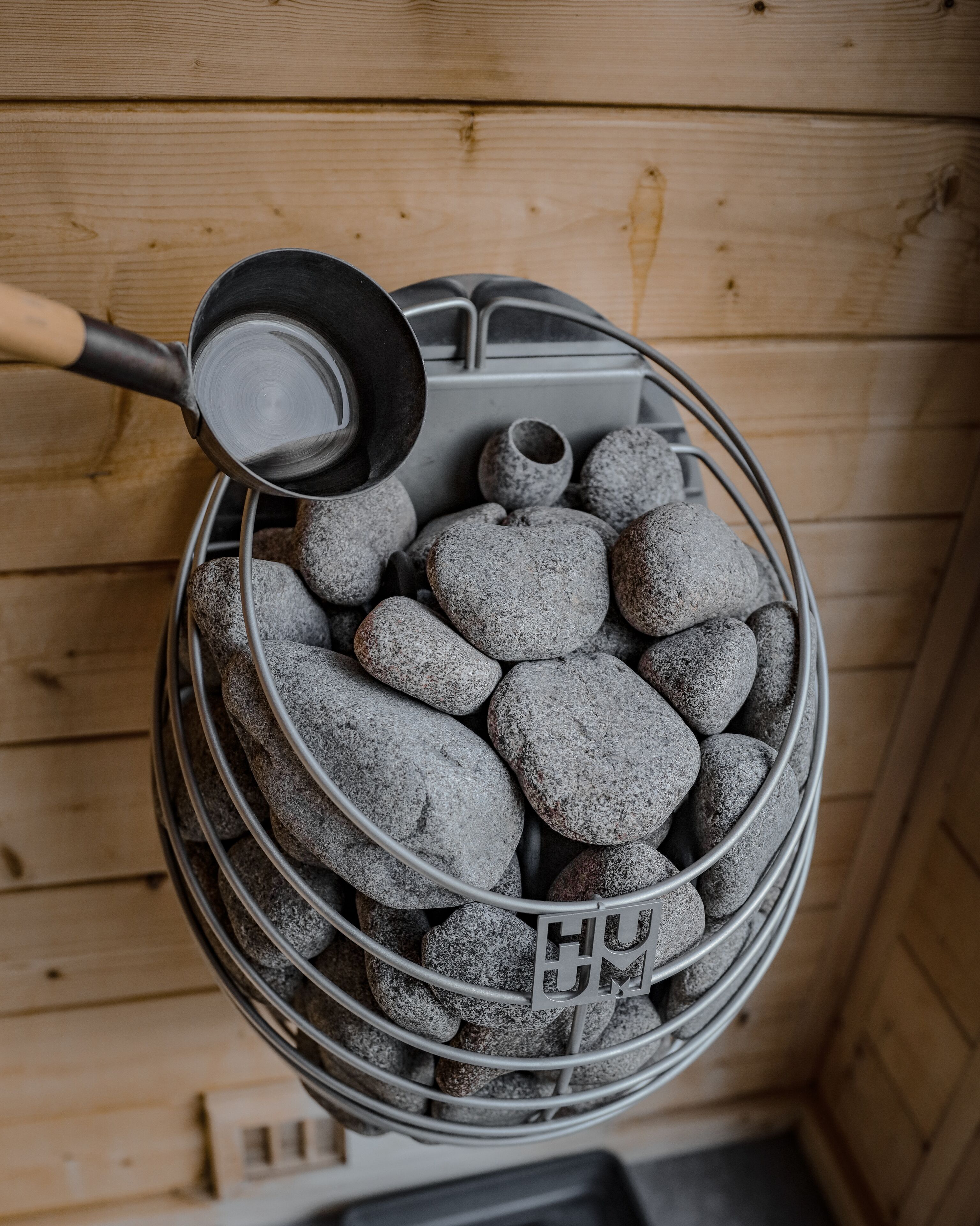 En korg av metall, fylld med grå stenar, placerad mot en trävägg.