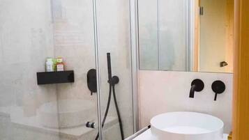 A modern bathroom with a glass-enclosed shower, a white sink, and a mirror above the sink.