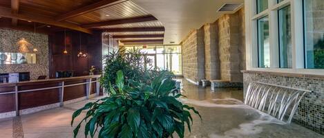 Een lobby met een receptiebalie, een grote potplant, een whirlpool met waterval en stenen muren.