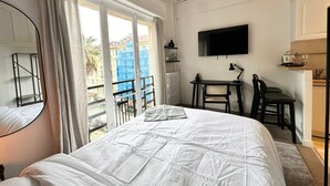 A bedroom with a large bed, a desk with a chair, a TV, and a view of the outside.