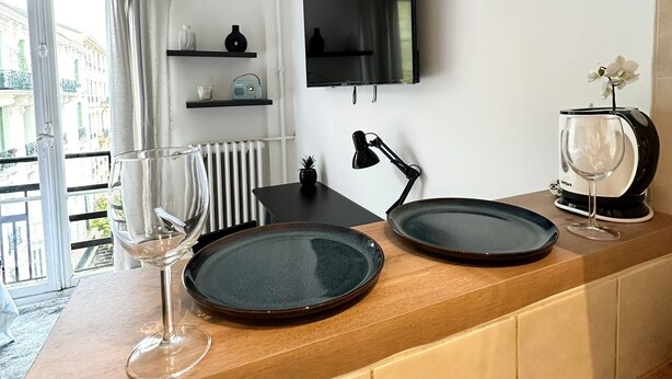 A modern kitchen with a wooden countertop, a flat-screen TV mounted on the wall, and a window with curtains.