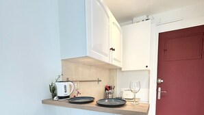 A compact kitchen with white cabinets, a wooden countertop, and two black chairs.