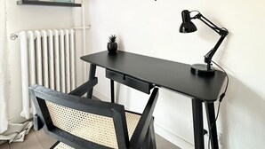 A modern workspace with a black desk, a chair, a TV mounted on the wall, and a radiator.