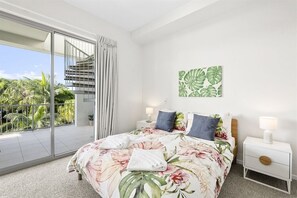 Ein Schlafzimmer mit Bett, Nachttischen, Blick ins Freie und einer Treppe.