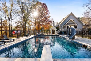 A swimming pool with lounge chairs, a slide, and a house in the background. - Sweet Tea & Serenity * Pool + Hot Tub * Fire Pit * Playground * (Mableton)