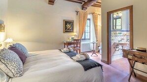 A bedroom with a large bed, a desk, a chair, and a bathroom visible through an open door. - Villa La Cappella  (Montespertoli)