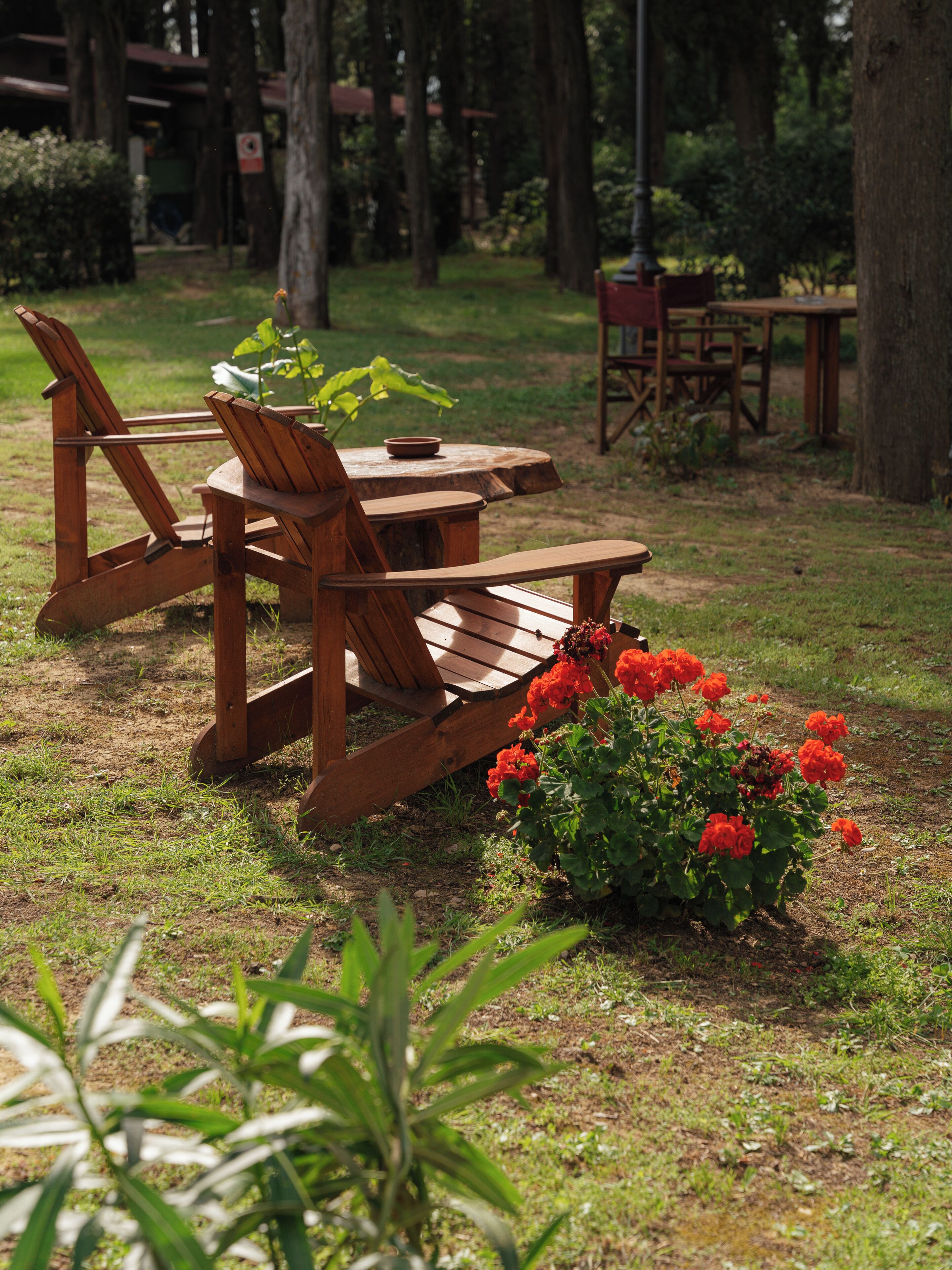 A wooden outdoor seating area with chairs and a table, surrounded by greenery and a flower bed.