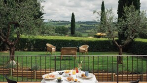 An outdoor dining area with a table set for breakfast, surrounded by chairs, overlooking a well-manicured garden and countryside. - Villa La Cappella  (Montespertoli)
