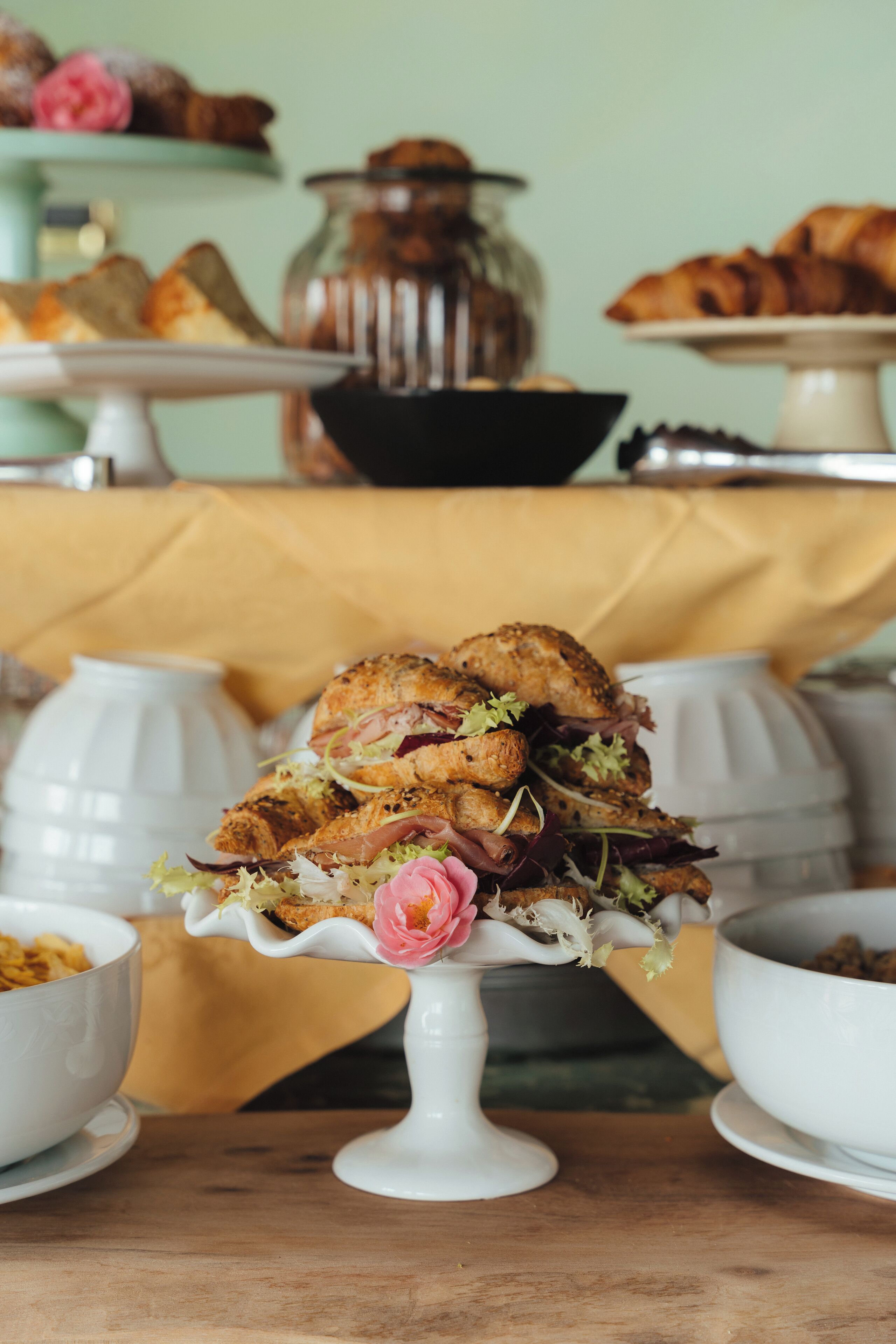 A table with a variety of food items, including a sandwich on a white stand, bowls, and a jar in the background.