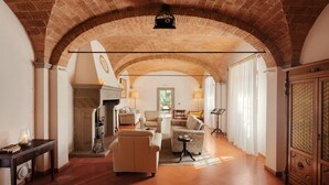 A spacious living room with a high arched brick ceiling, a fireplace, and a view through an open doorway. - Villa La Cappella  (Montespertoli)