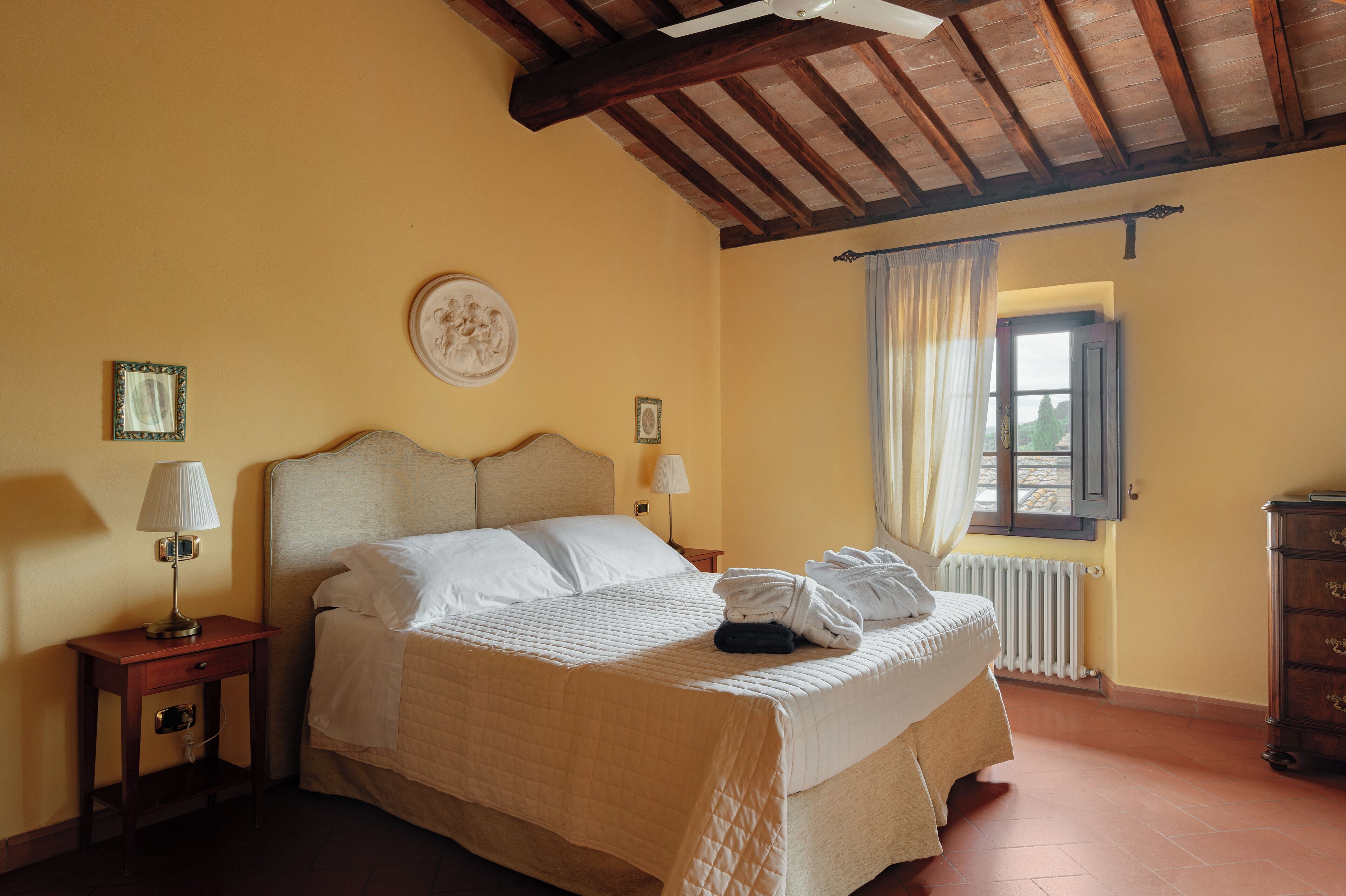 A hotel room with a bed, a nightstand, a lamp, a window with curtains, and a radiator.