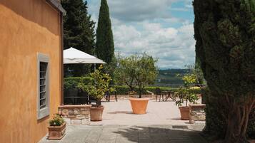 An outdoor patio with stone flooring, potted plants, a white umbrella, and a view of the countryside.