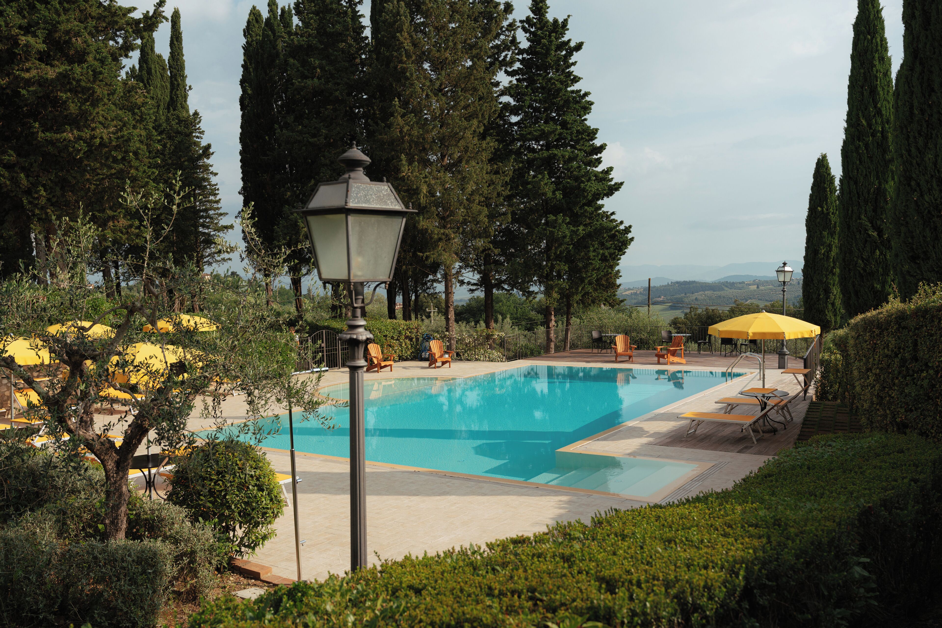 Una piscina rodeada de vegetación, con una farola y mobiliario de exterior.