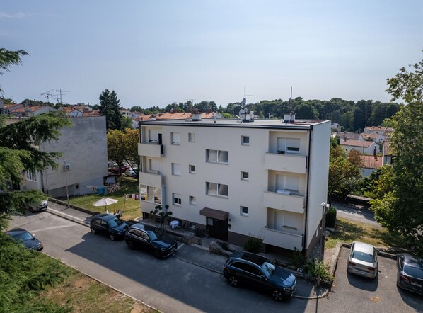 A multi-story residential building with balconies, a parking area with several cars, and a clear view of the surrounding neighborhood. - Premium Apartment With Patio (Porec)