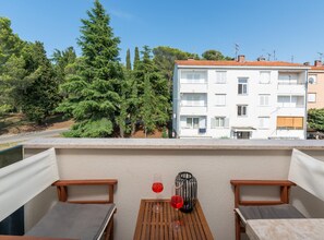 A balcony with a table, two chairs, and a view of a building with multiple windows and a red-tiled roof. - Premium Apartment With Patio (Porec)