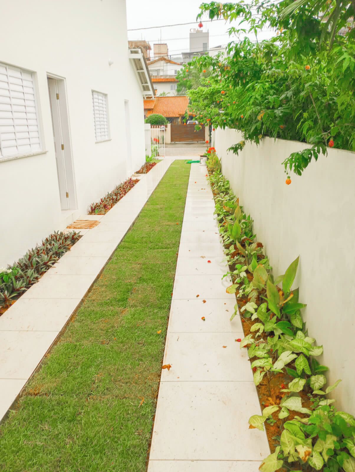 Un estrecho sendero bordeado por muros blancos y un césped verde, que conduce a la entrada de un edificio.