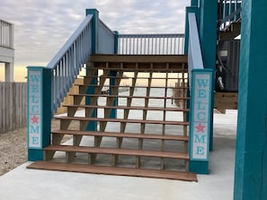 Uma escadaria de madeira com uma placa que diz 'WELCOME' no topo, levando a um terraço.