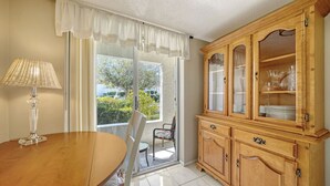Zona pranzo con tavolo in legno, lampada, sedia, credenza con ante in vetro e vista dalla finestra.