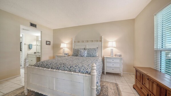 A bedroom with a bed, nightstands, a dresser, a mirror, and a window with blinds.