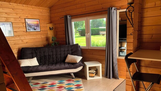 A cozy cabin interior with a sofa, a small table, a colorful rug, and a dining area. - Charming vacation home in the middle of nature near Kühlungsborn  (Kröpelin)
