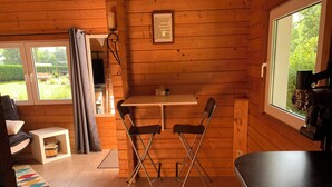 A cozy cabin interior with wooden walls, a dining area with two chairs, a small table, and a window with a view of greenery. - Charming vacation home in the middle of nature near Kühlungsborn  (Kröpelin)