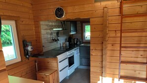 A compact kitchen with wooden walls, a sink, a stove, and a window. - Charming vacation home in the middle of nature near Kühlungsborn  (Kröpelin)