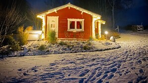 A snow-covered landscape with a red house illuminated by lights, surrounded by bare trees and a clear sky. - Charming vacation home in the middle of nature near Kühlungsborn  (Kröpelin)