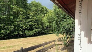 A view of a grassy field with a wooden fence and a stone pathway leading to a white building with a red roof. - Charming vacation home in the middle of nature near Kühlungsborn  (Kröpelin)
