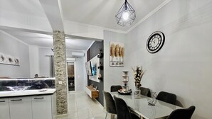 Une cuisine moderne avec un pare-feu en marbre, un coin repas doté d’une table en verre et de chaises noires, et une horloge murale.