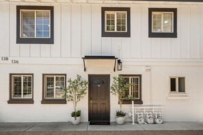 A two-story building with a dark brown front door, potted plants, and a bench.