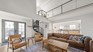 A spacious living area with a high ceiling, a staircase, a brown leather sofa, a wooden coffee table, and a patterned rug. - Walkable Downtown Spa Retreat (Bend)