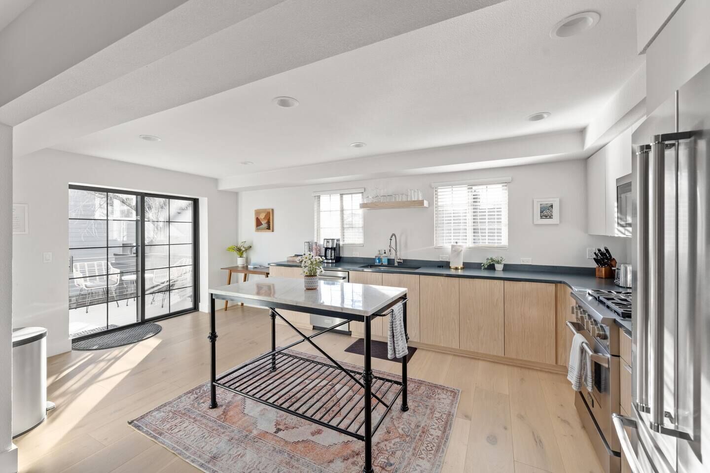 A modern kitchen with a central island, a dining area with a table, and a large sliding glass door leading to an outdoor space.