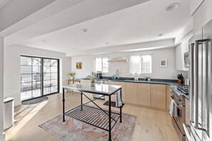 A modern kitchen with a central island, a dining area with a table, and a large sliding glass door leading to an outdoor space. - Walkable Downtown Spa Retreat (Bend)