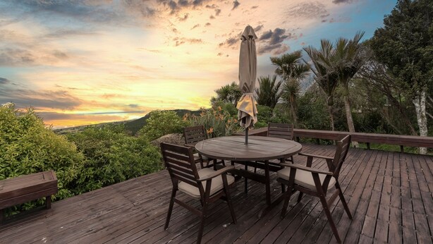 Una terraza de madera con una mesa redonda y sillas, rodeada de exuberante vegetación y vistas al paisaje.