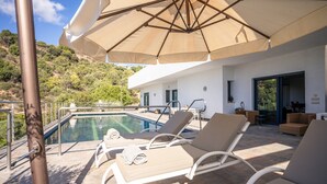 A poolside area with lounge chairs, a large umbrella, and a view of the pool and hillside. - Lavish Villa With Private Pool (Marbella)