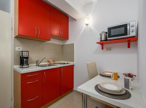 A compact kitchen with red cabinets, a microwave, a coffee maker, and a dining table set with plates and cups.