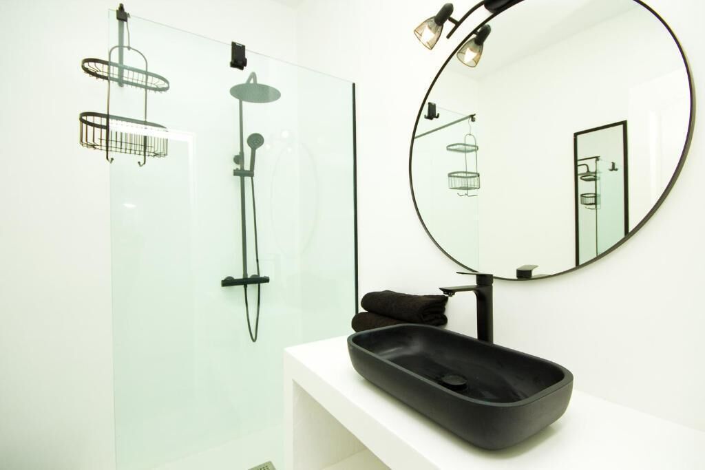 A modern bathroom with a glass shower enclosure, a round mirror, and a black sink.