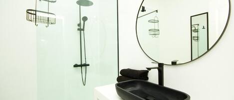 A modern bathroom with a glass shower enclosure, a round mirror, and a black sink.