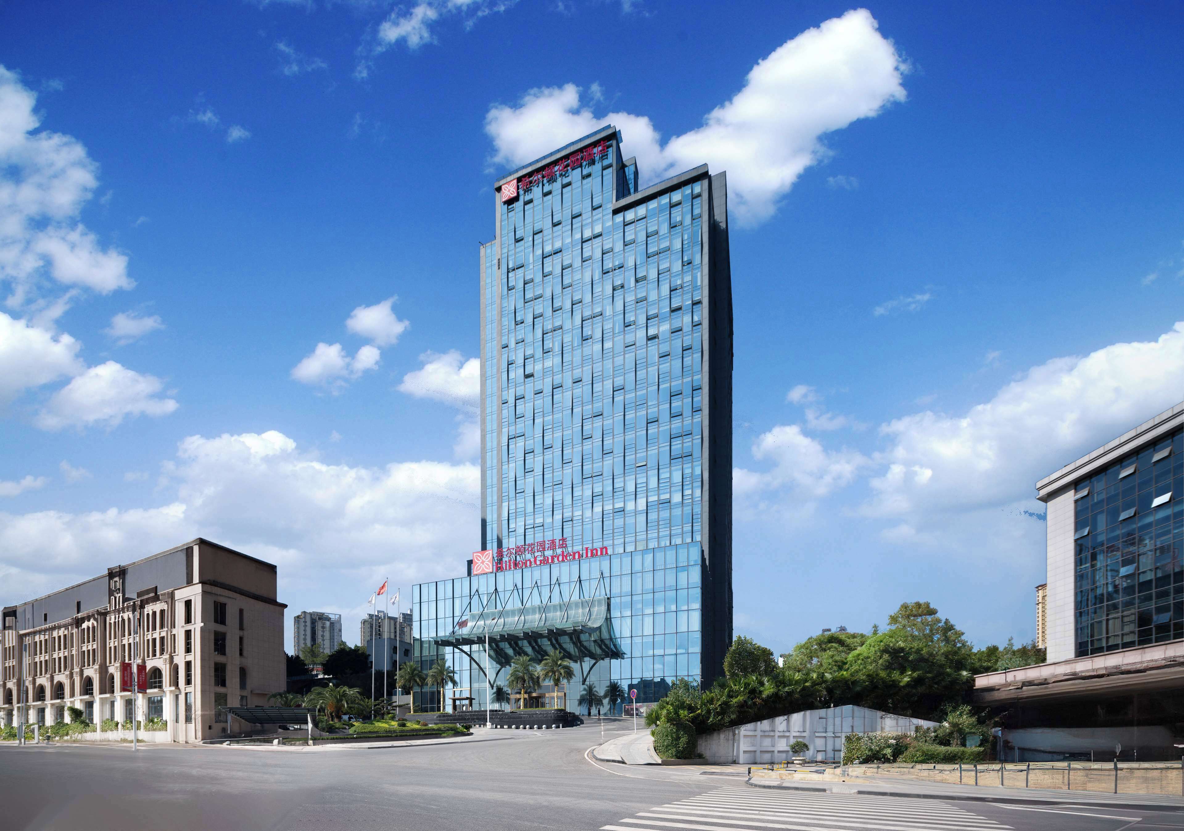 A tall, modern hotel with a glass facade, a prominent entrance with a canopy, and a clear blue sky in the background.