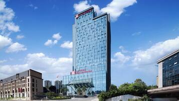 A tall, modern hotel with a glass facade, a prominent entrance with a canopy, and a clear blue sky in the background.
