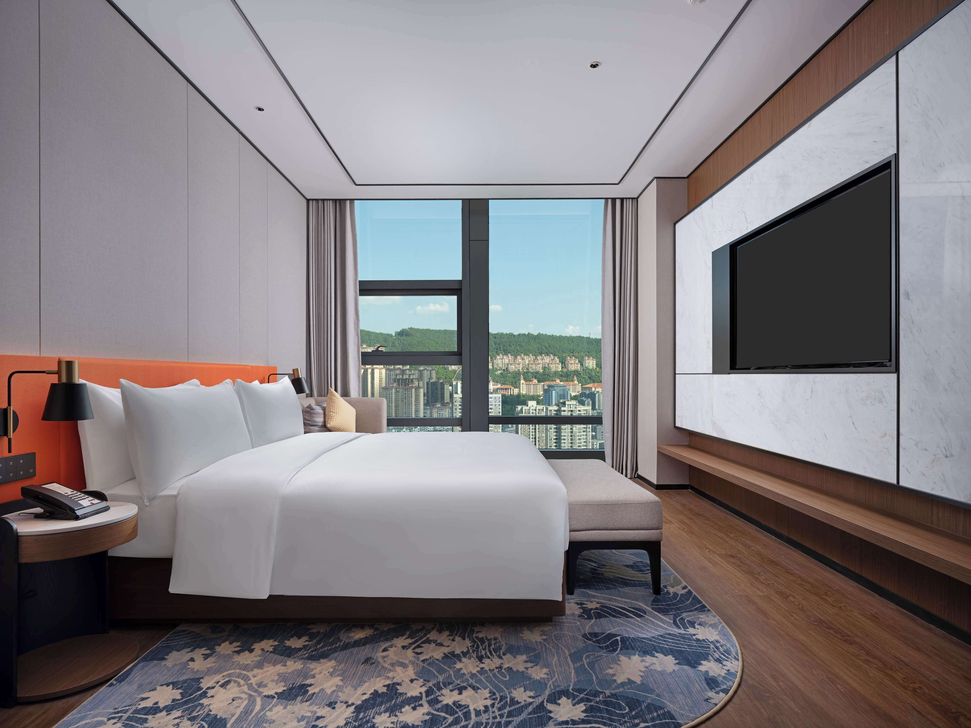 A modern hotel room with a large bed, a TV, and a city view.