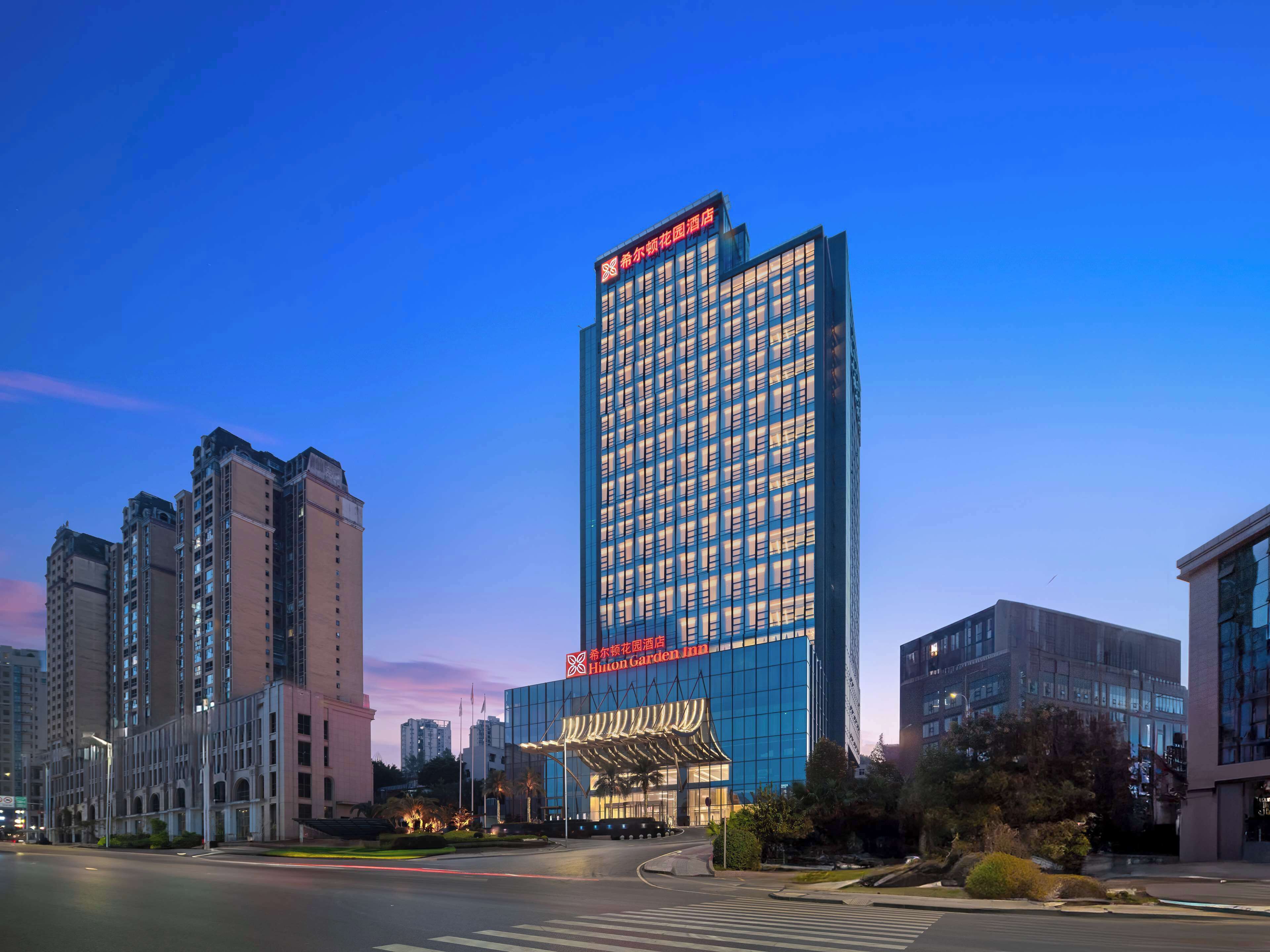 A modern hotel with a prominent Hilton Garden Inn sign, surrounded by high-rise buildings.