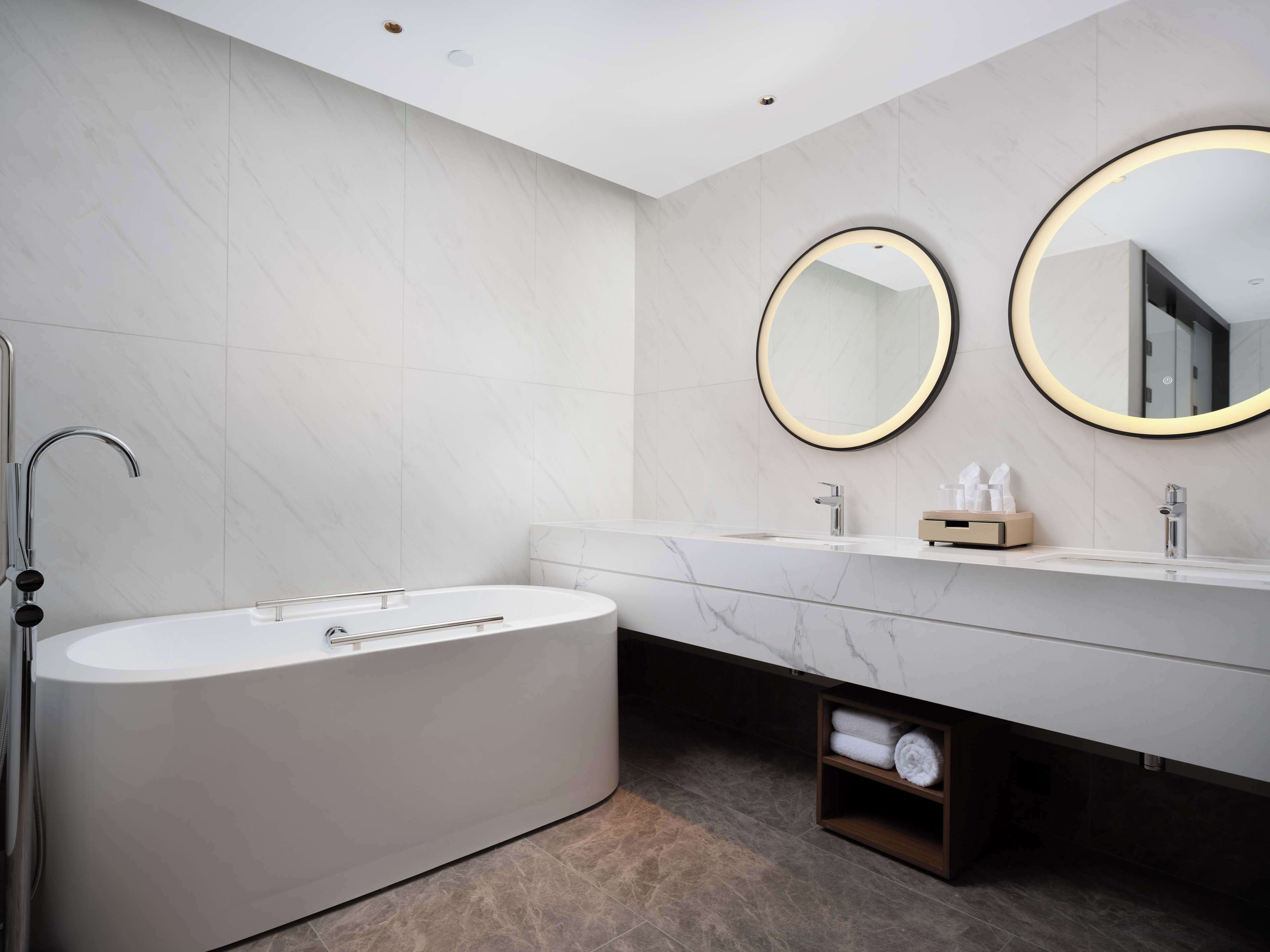 A modern bathroom with a freestanding bathtub, two sinks with round mirrors, and a towel rack.