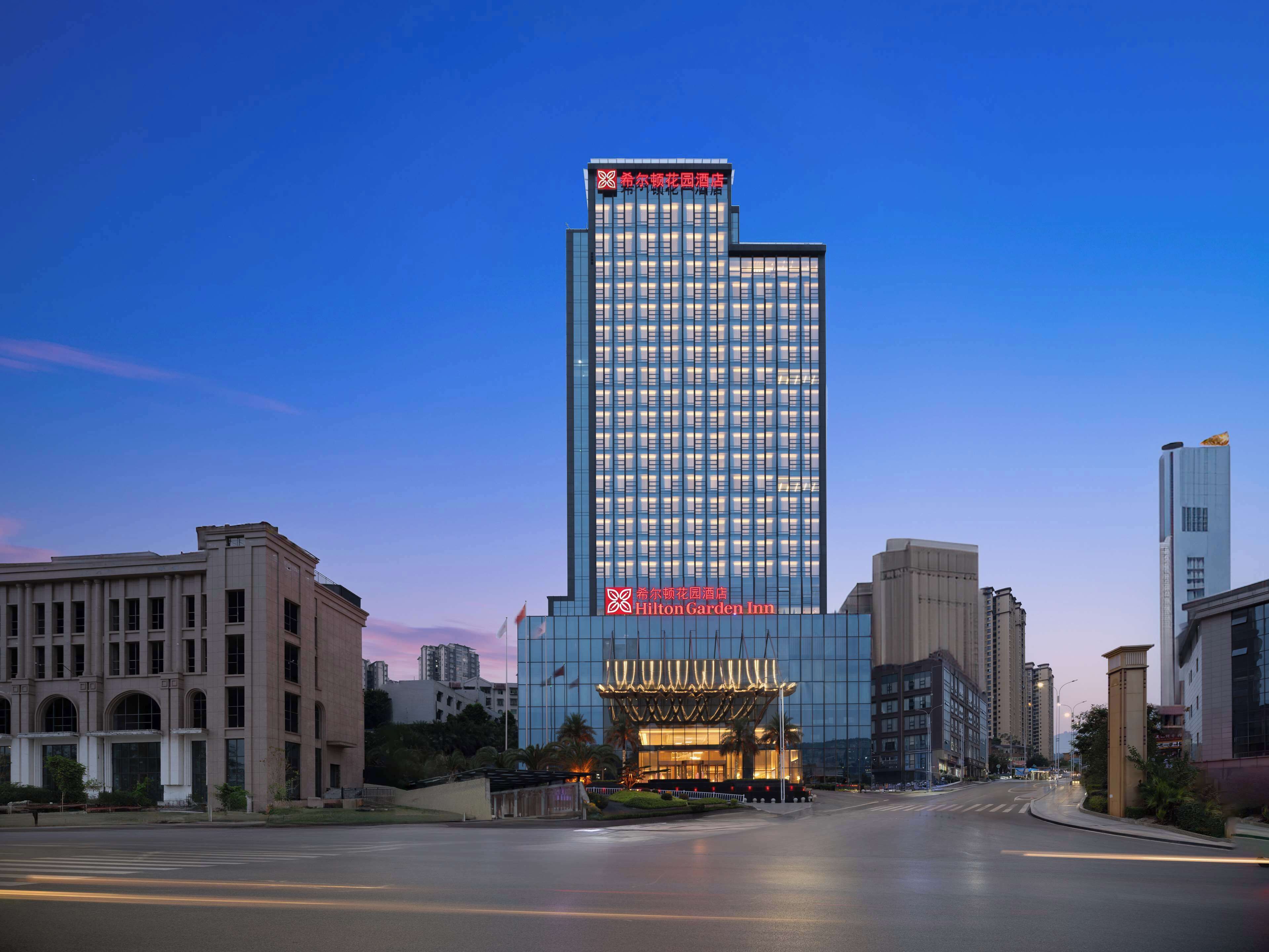 A modern hotel with a prominent glass facade and a sign indicating it is the Hilton Garden Inn.