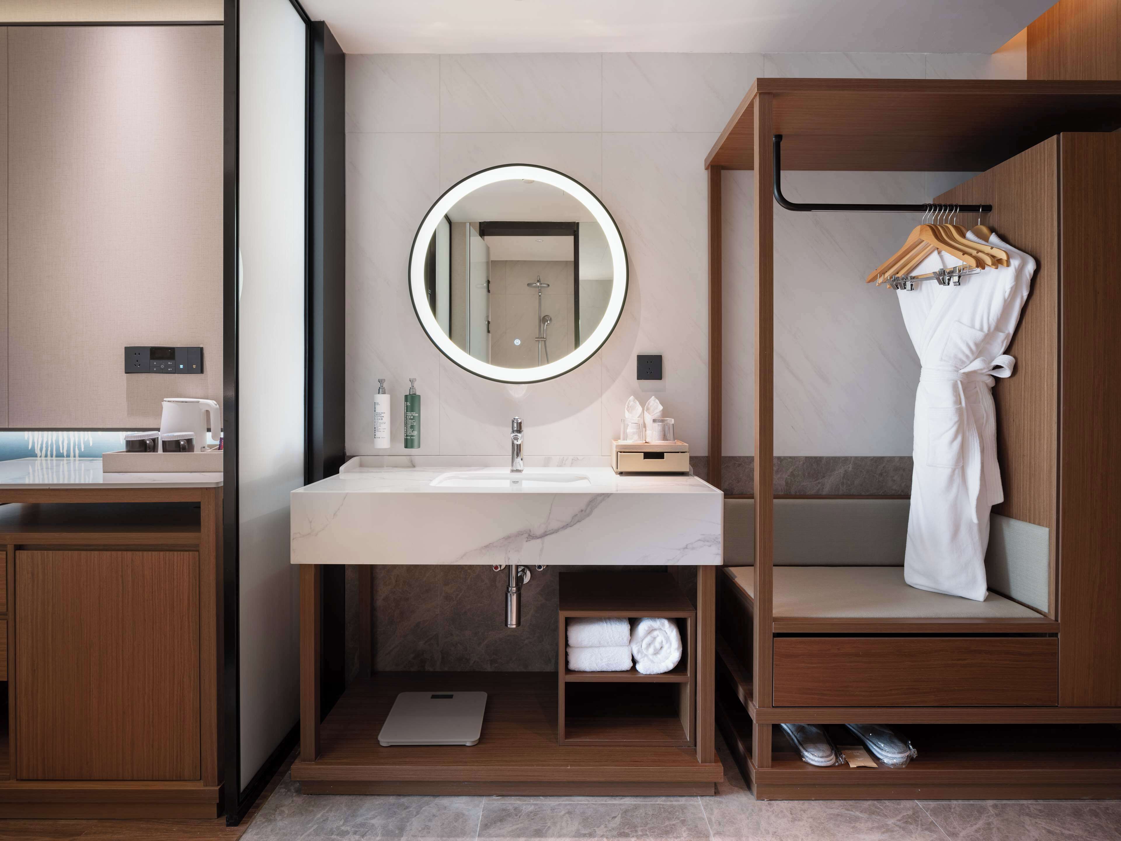 A modern bathroom with a large mirror, a sink, and a robe rack.