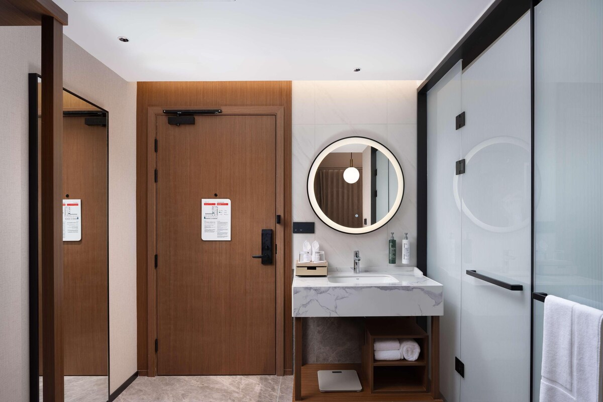 Een moderne badkamer met een houten deur, een marmeren wastafel, een spiegel en een handdoekhouder.