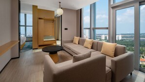 A modern living room with a sofa, a coffee table, and a view of the city through large windows. - Hilton Garden Inn Danzhou Yangpu (Danzhou)