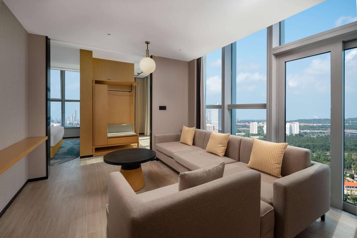 A modern living room with a sofa, a coffee table, and a view of the city through large windows.