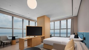 A modern hotel room with a large bed, a TV, a desk, and a view of the sea. - Hilton Garden Inn Danzhou Yangpu (Danzhou)