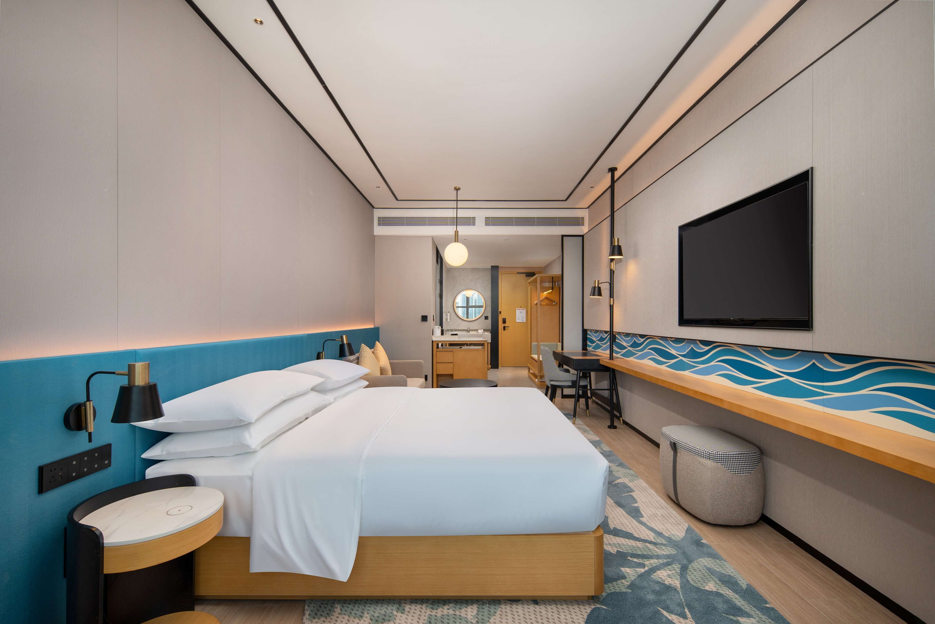 A modern hotel room with a large bed, a desk, a chair, a TV, and a bathroom.